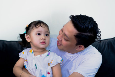 Father and daughter bonding, playing together, lying on sofa in family room.