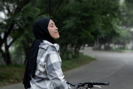 Muslim Woman Smiling on Bike with Headphones, Street View, angle from the right back. Healthy and...