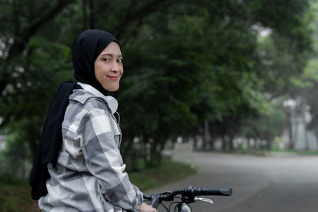 Muslim Woman Smiling on Bike with Headphones, Street View, angle from the right back. Healthy and...