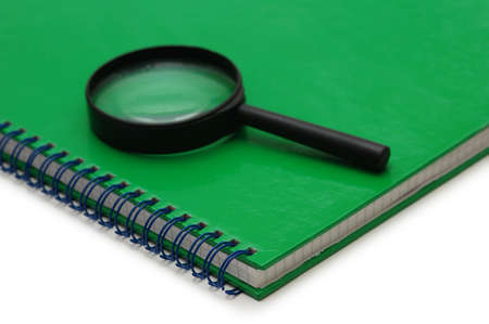 Magnifying glass over the green notebook isolated on whiteの写真素材