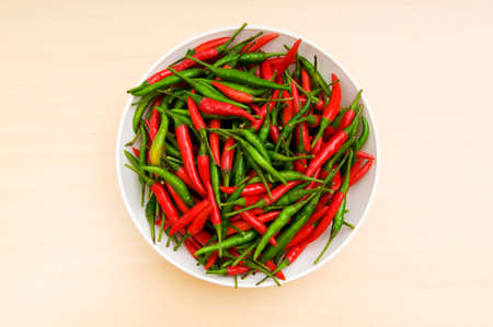Hot peppers in the plate on wooden tableの写真素材