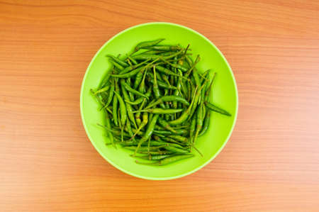 Hot peppers in the plate on wooden tableの写真素材