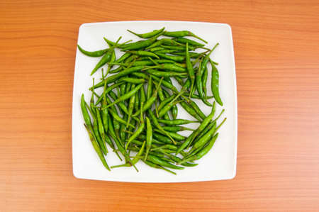 Hot peppers in the plate on wooden tableの写真素材