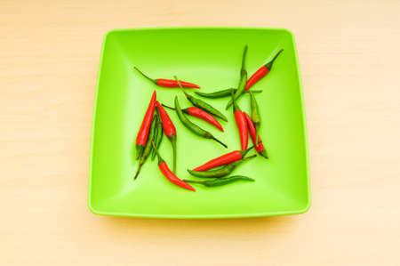 Hot peppers in the plate on wooden tableの写真素材