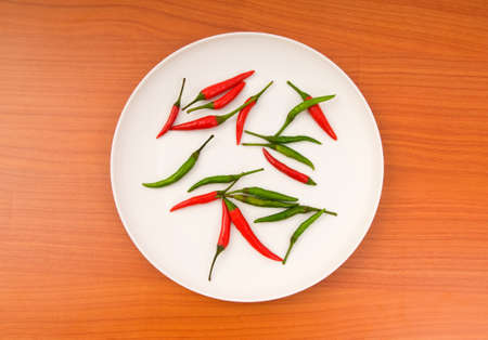 Hot peppers in the plate on wooden tableの写真素材
