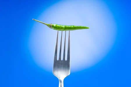Hot pepper on the fork against colour backgroundの写真素材