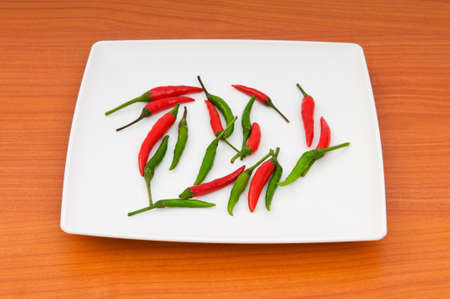 Hot peppers in the plate on wooden tableの写真素材