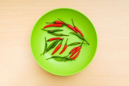 Hot peppers in the plate on wooden tableの写真素材