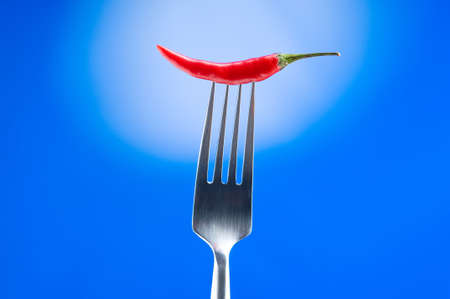 Hot pepper on the fork against colour backgroundの写真素材