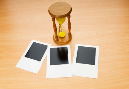 Blank instant photos and hour glass on the wooden tableの写真素材