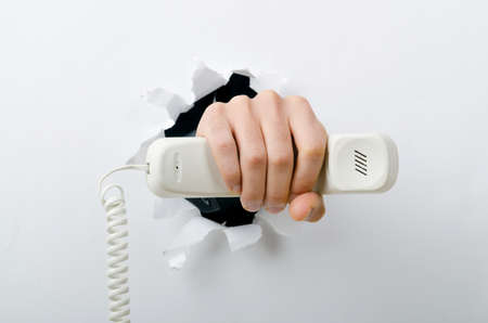 Hand holding phone through hole in paperの写真素材