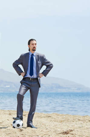 Businessman with football on beachの写真素材