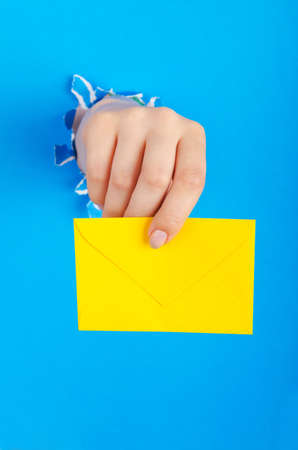Hand holding paper envelope from holeの写真素材