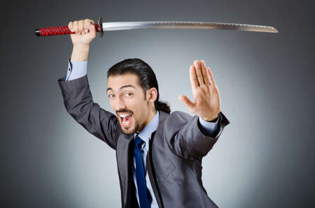 Angry businessman with sword in dark roomの写真素材