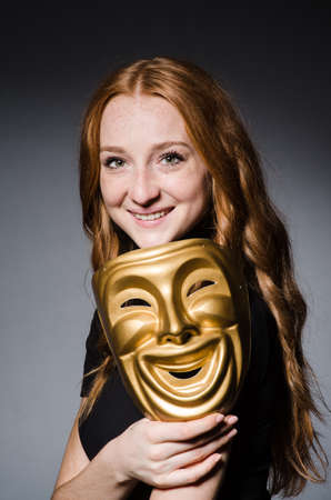 Redhead woman iwith mask in hypocrisy consept against grey backgroundの写真素材