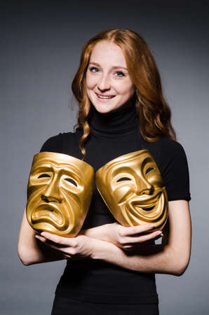 Redhead woman iwith masks in hypocrisy consept against grey backgroundの写真素材