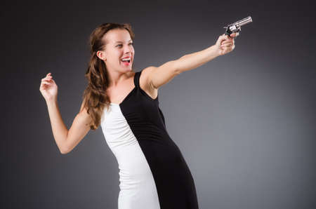 Woman with gun against dark backgroundの写真素材