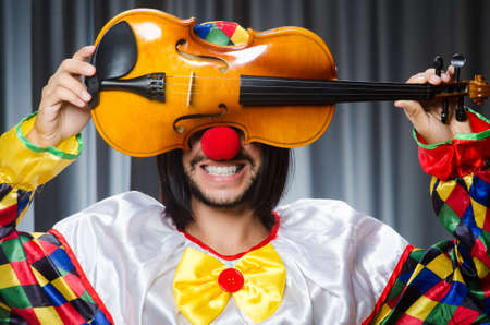 Funny clown plyaing violin against curtain