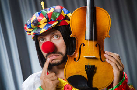Funny clown plyaing violin against curtain