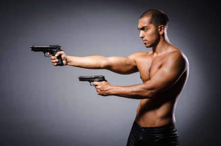Ripped man with gun against grey backgroundの写真素材