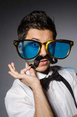 Young man with false moustache and large sunglasses isolated on grayの写真素材