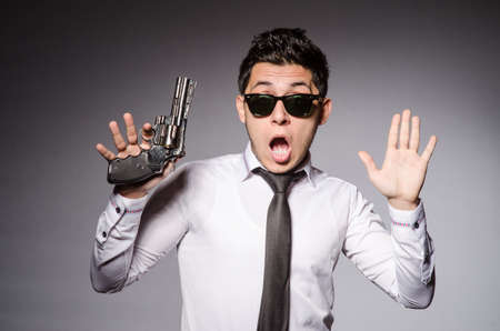 Young man in cool sunglasses holding gun isolated on grayの写真素材
