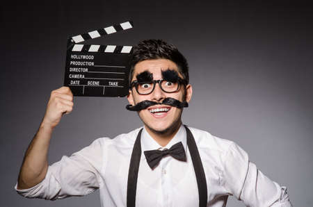 Young man with false moustache holding clapperboard isolated on grayの写真素材