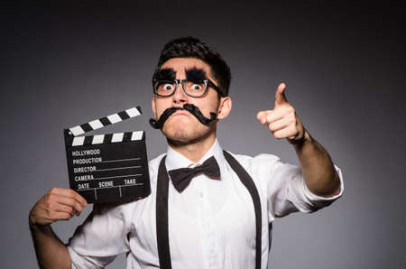 Young man with false moustache holding clapperboard isolated on grayの写真素材