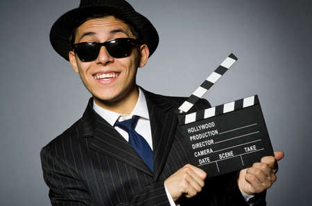 Young man in elegant suit holding clapperboard against grayの写真素材