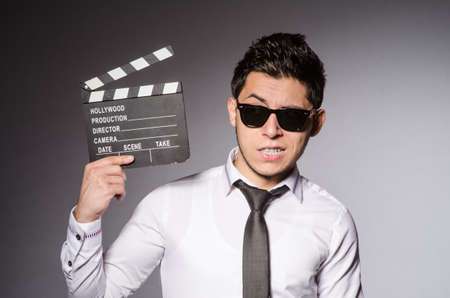 Young caucasian man with clapperboard against gray