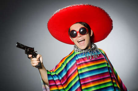 Man in vivid mexican poncho holding handgun against grayの写真素材