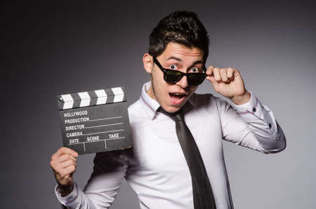 Young caucasian man with clapperboard against gray