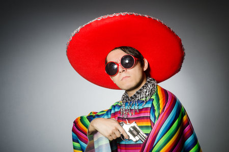 Man in vivid mexican poncho holding handgun against grayの写真素材