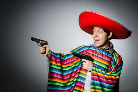 Man in vivid mexican poncho holding handgun against grayの写真素材