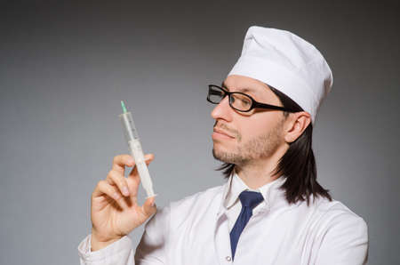 Male doctor holding syringe against grayの写真素材