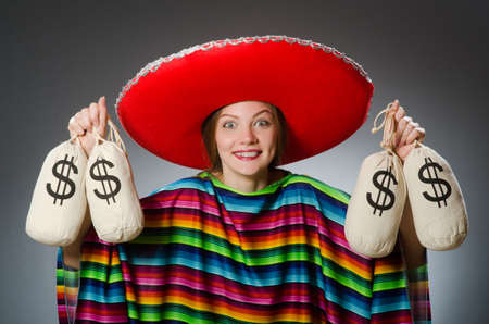 Girl in mexican vivid poncho holding money bags against grayの写真素材