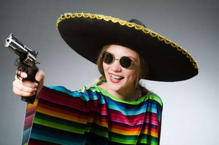 Girl in mexican vivid poncho with handgun against grayの写真素材
