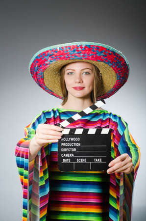 Girl in mexican vivid poncho holding clapboard against grayの写真素材