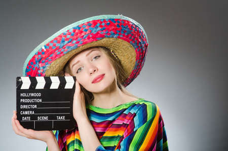 Girl in mexican vivid poncho holding clapboard against grayの写真素材