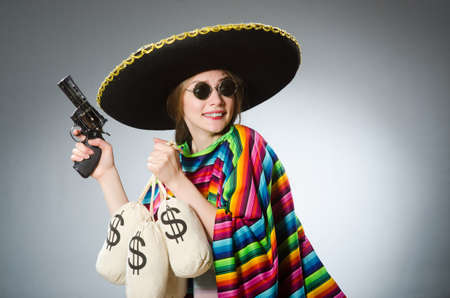Girl in mexican poncho holding handgun and money sacks against grayの写真素材