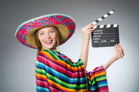 Girl in mexican vivid poncho holding clapboard against grayの写真素材