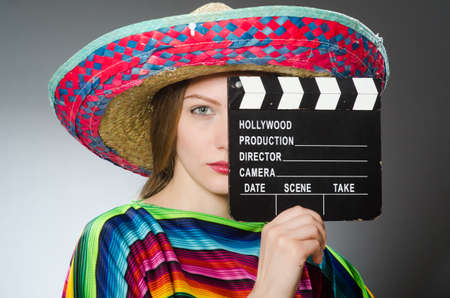Girl in mexican vivid poncho holding clapboard against grayの写真素材
