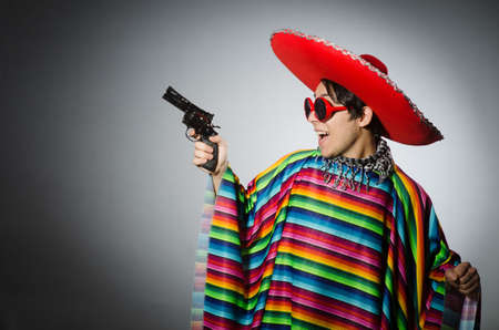 Man in vivid mexican poncho holding handgun against grayの写真素材