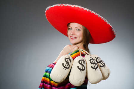 Girl in mexican vivid poncho holding money bags against grayの写真素材