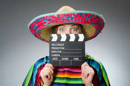 Girl in mexican vivid poncho holding clapboard against grayの写真素材
