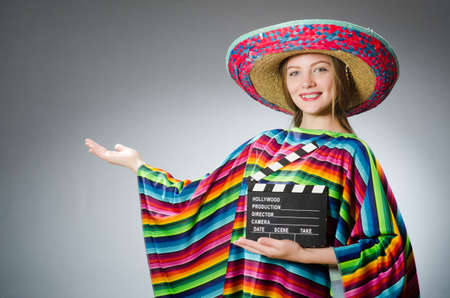 Girl in mexican vivid poncho holding clapboard against grayの写真素材