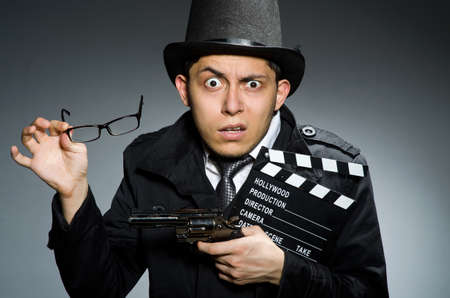 Young man with weapon and clapboard against grayの写真素材