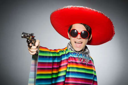 Man in vivid mexican poncho holding handgun against grayの写真素材