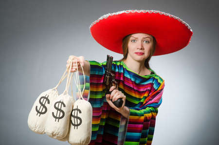 Girl in mexican poncho holding handgun and money sacks against grayの写真素材