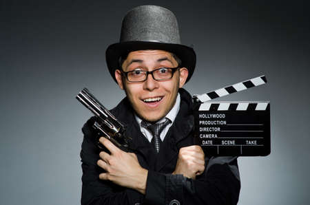 Young man with weapon and clapboard against grayの写真素材